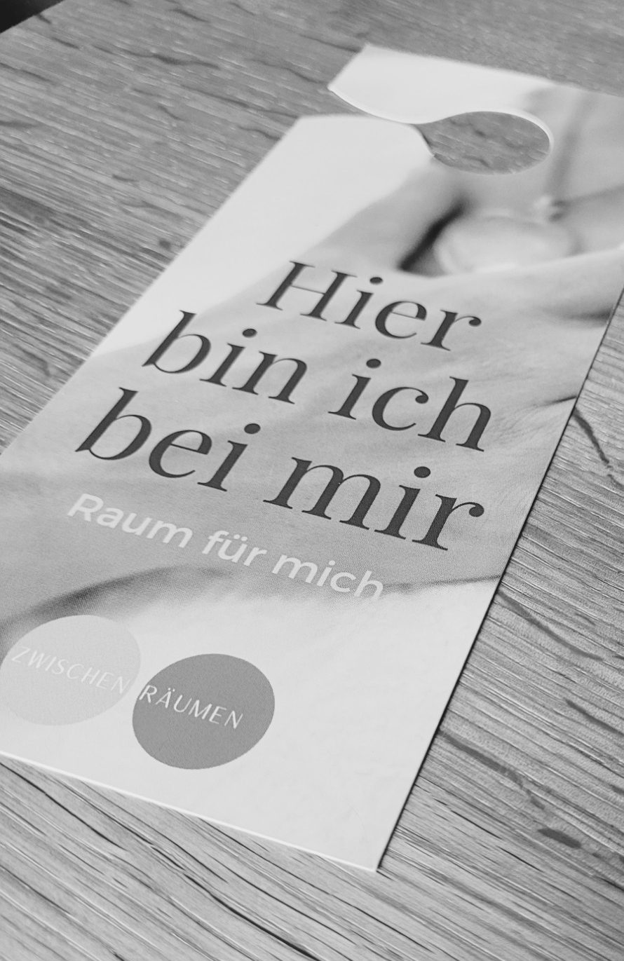 Gedruckte Karte bzw. Türanhänger mit der Aufschrift ‚Hier bin ich mir. Raum für mich‘ liegt auf einem Holztisch.